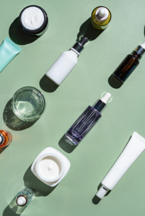 Different glass bottles with serum or oil and cosmetic skin care cream on green background. Trending shadow. Cosmetic mockup. Top view with copy space. Flat lay.
